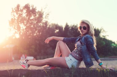 oturma ve günbatımı güneşli açık havada dikey poz güzel moda genç kadın güneş gözlüğü.
