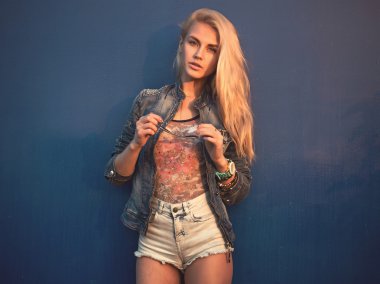 Açık yaz portre portre genç şık moda çekici kadın veya kız sokak Kot ceket ve güneş gözlüğü güneşli gün içinde mavi duvara yakın dururken elleri
