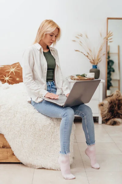 Ung kvinna sitter på sängen med bärbar dator — Stockfoto