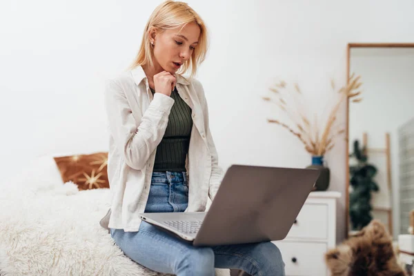 Ung kvinna sitter i en fåtölj med bärbar dator — Stockfoto