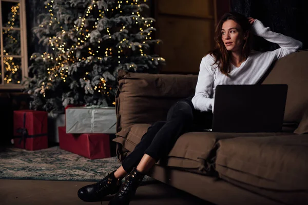 Winter weekend, jonge vrouw thuis door kerstboom met laptop op de bank — Stockfoto