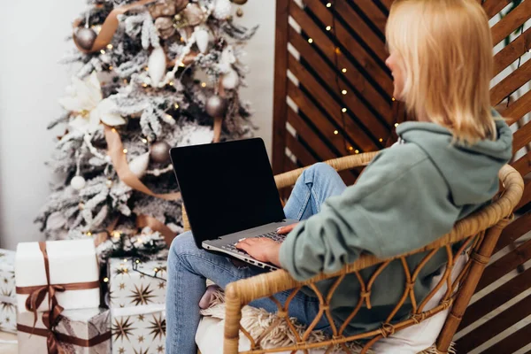 Mladá žena sedí v křesle s notebookem na Vánoce — Stock fotografie