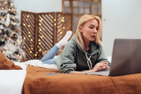 Jovem mulher usando computador portátil enquanto deitada no sofá em casa. — Fotografia de Stock