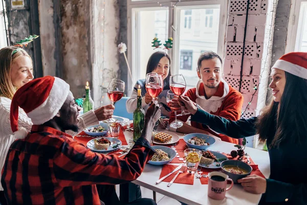Gente celebrando sentada en la mesa, tintineando vasos. Nochebuena o Año Nuevo . —  Fotos de Stock