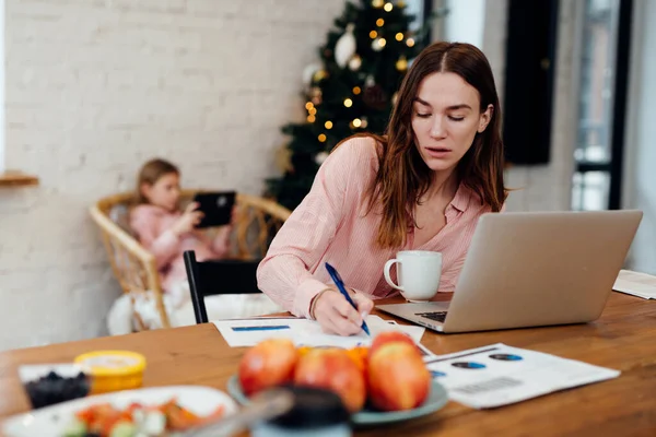 A fiatal nő otthon dolgozik, míg a lánya otthon tölti a téli vakációt. — Stock Fotó