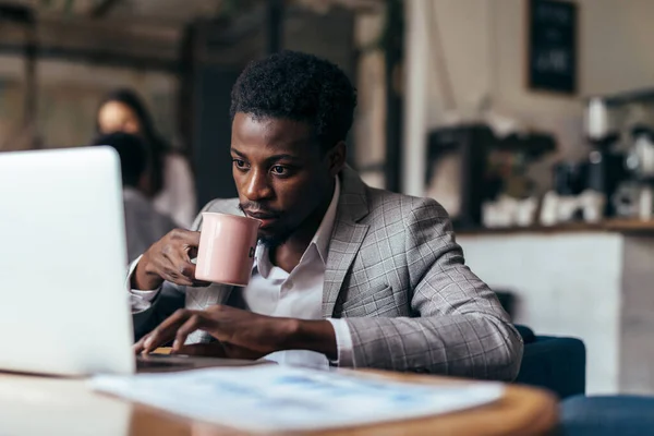 Hombre negro en la cafetería con el ordenador portátil de trabajo, beber café. —  Fotos de Stock