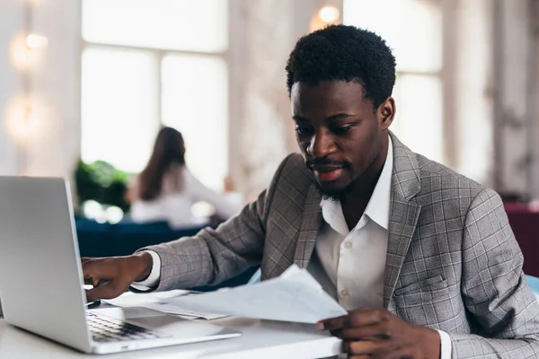 El hombre negro se sienta a la mesa y trabaja sosteniendo el documento en su mano. —  Fotos de Stock