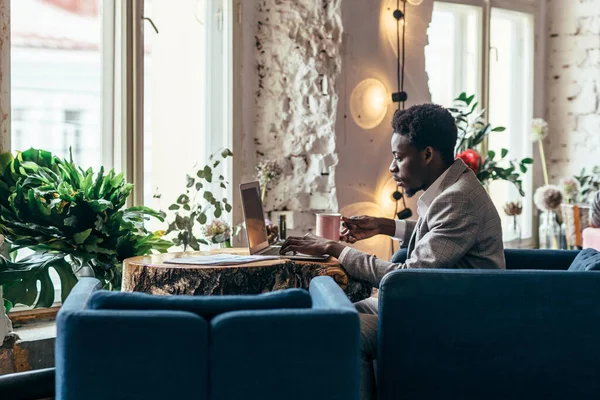 Mann benutzt Laptop während er im Café sitzt. Junger Afroamerikaner arbeitet am Laptop. — Stockfoto