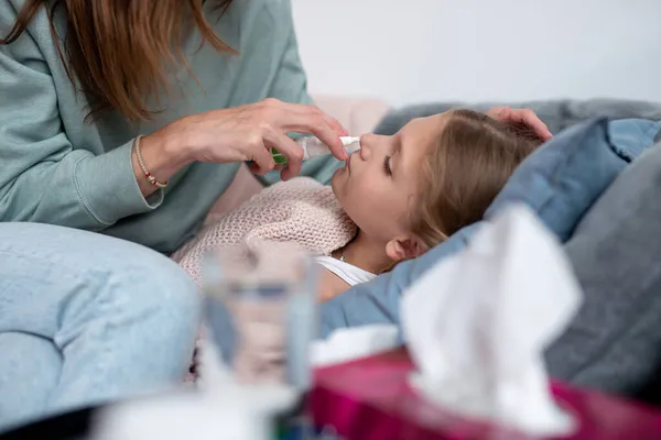Мать брызгает носовые лекарства в нос своей больной дочери. — стоковое фото