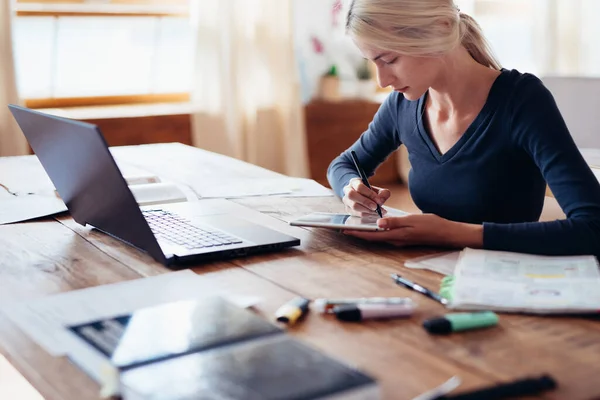 Ung kvinna sitter vid bordet gör uppdrag hemma. — Stockfoto