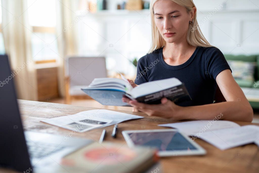 Woman student sitting at table reading book.