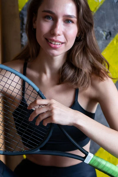 Portrait of female tennis player with racket sitting on gym floor — Zdjęcie stockowe