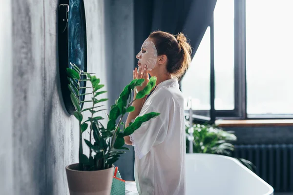 Woman in bathroom with mask on face in front of mirror — Stockfoto