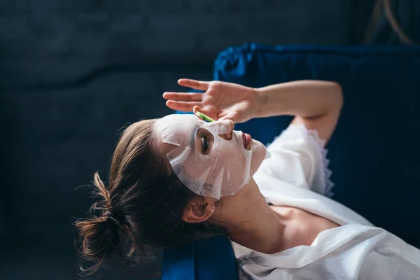 Kanepede yüzü çarşaf maskeli ve salatalık dilimli bir kadın yatıyor. — Stok fotoğraf