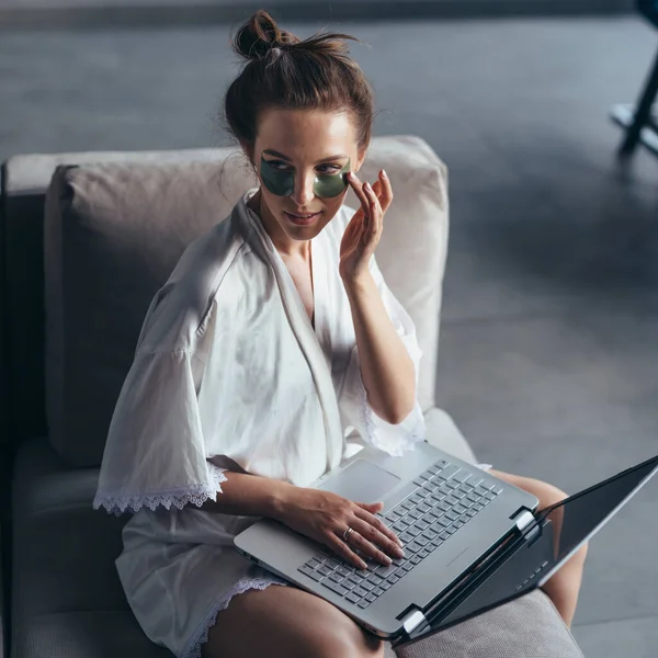 Woman sits at home on the couch in a nightgown with a laptop — Stock Photo, Image