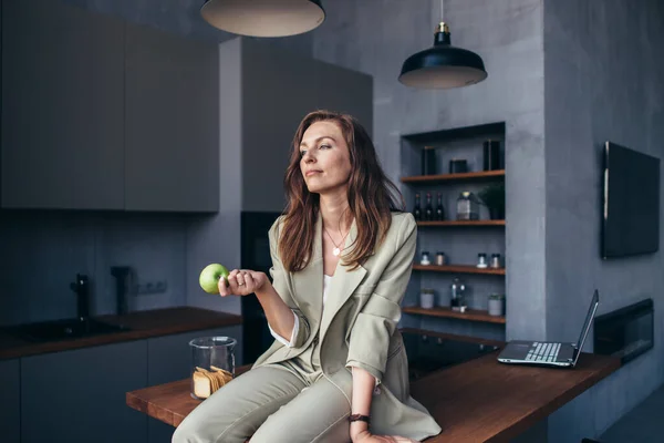 Vrouw zit in de keuken met een appel tijdens een pauze — Stockfoto