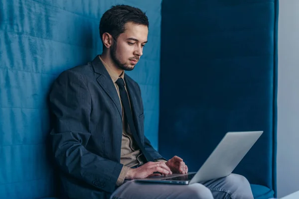 Portret van een jonge zakenman die op een laptop werkt terwijl hij alleen in een kantoorhokje zit. — Stockfoto