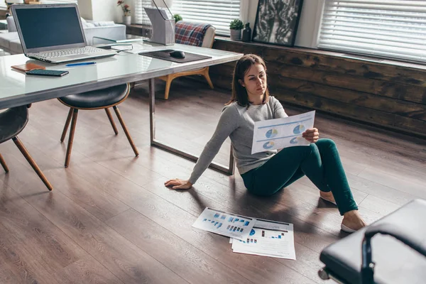 Kvinnan sitter på golvet på kontoret och tittar på diagrammen på bladet — Stockfoto