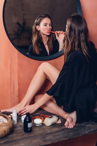 Mujer cepillándose los dientes por la noche frente al espejo — Foto de Stock