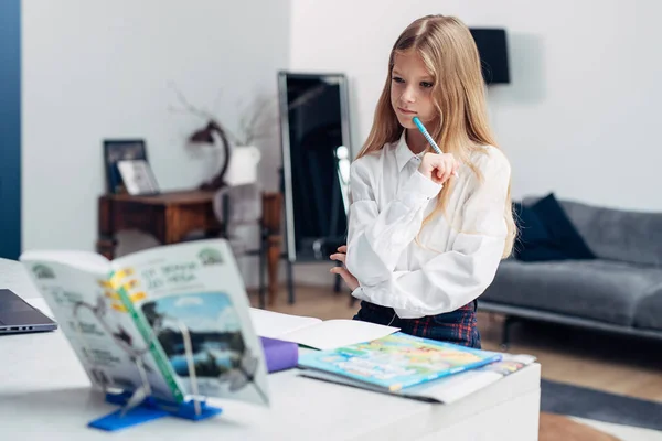 女の子は宿題をしながら教科書をよく見る — ストック写真