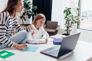 Kız ödevini yapıyor, annesi yanına oturuyor.