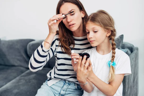 Mutter trägt Wimpern mit Wimperntusche auf und schaut in kleinen Spiegel ihrer Töchter — Stockfoto