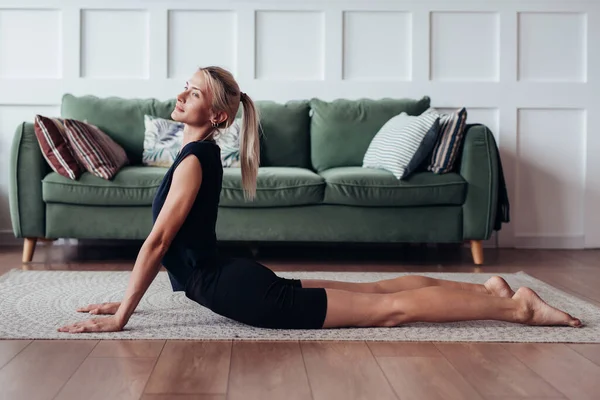 Mujer joven haciendo ejercicio en casa haciendo un ejercicio para la flexibilidad de la espalda. — Foto de Stock