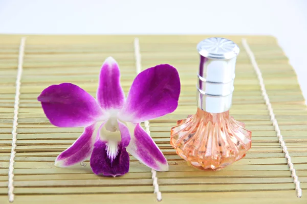 Purpurowa orchidea i pomarańczowy perfum butelek w bambus naczynie — Zdjęcie stockowe