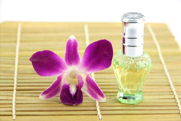 Фиолетовая орхидея и зеленые флаконы духов в бамбуковой тарелке — стоковое фото
