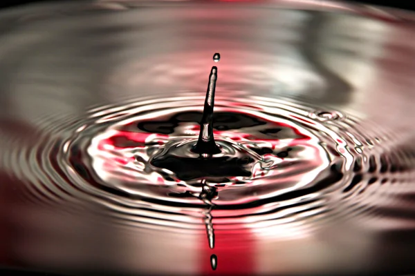 Röd bakgrund vatten droppar en vacker form i bassängen. — Stockfoto