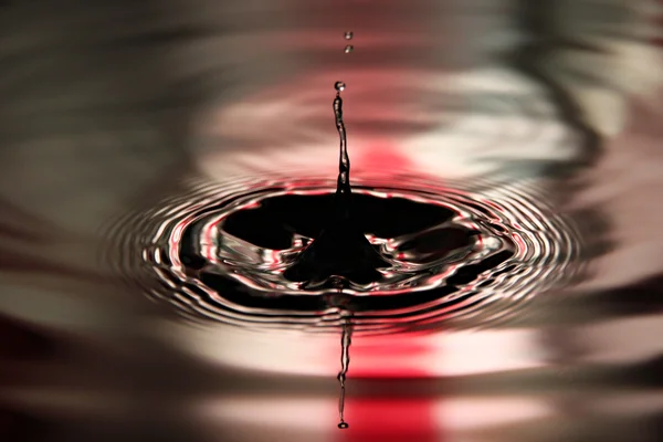 Piros háttérben a víz csepp egy szép alak medencéjében. — Stock Fotó