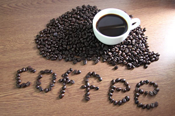 Ceașcă albă de cafea care se odihnește pe boabe de cafea și text Cafea pe lemn — Fotografie, imagine de stoc