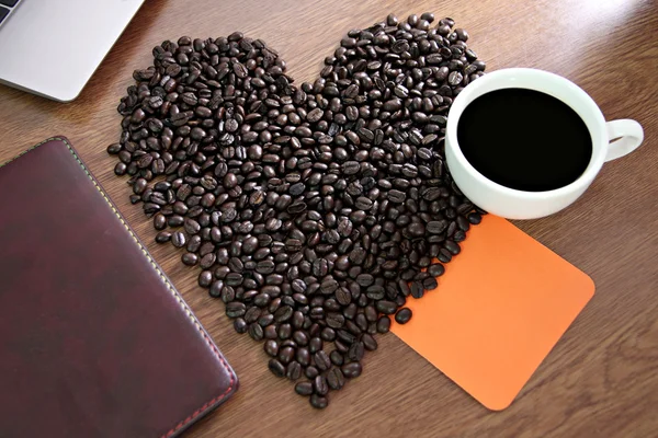 Granos de café dispuestos una forma de corazón y papel colocado Cuaderno wi — Foto de Stock