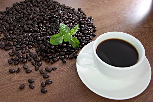Kaffeebohnen und grüne Pfefferminze neben einer weißen Kaffeetasse. — Stockfoto