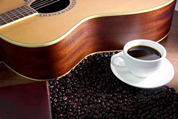 White coffee cup resting on guitar and coffee beans. — Stock Photo, Image