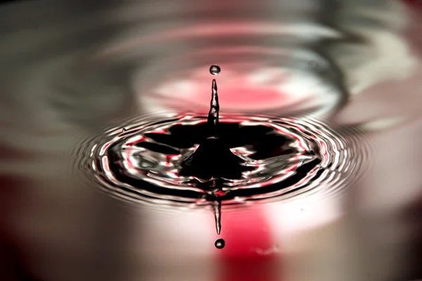 Röd bakgrund vatten droppar en vacker form i bassängen. — Stockfoto