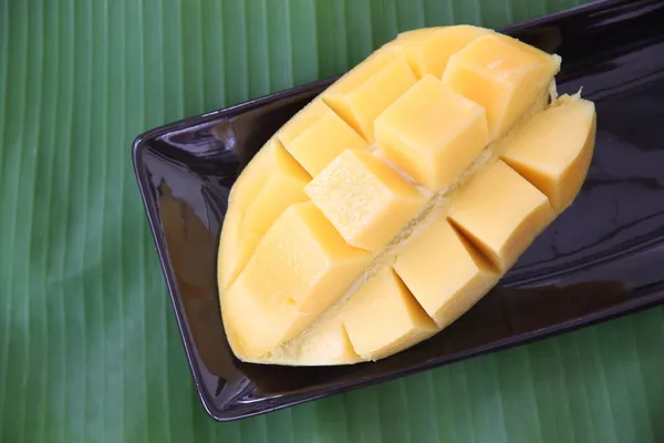 Rijpe mango met segmenten in zwarte schotel op banaan verlaat. — Stockfoto