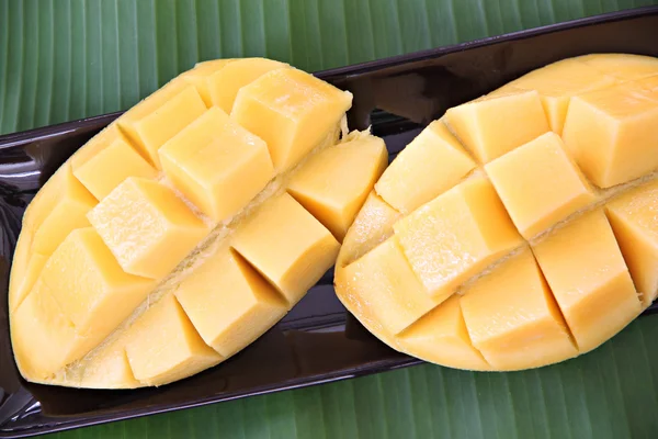 Rijpe mango met segmenten in zwarte schotel op banaan verlaat. — Stockfoto