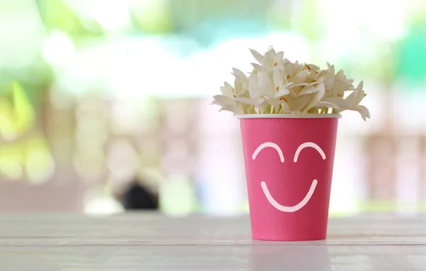 Pink paper cup with a smile symbol and white flowers blooming on top cup and have copy space for design in your work.