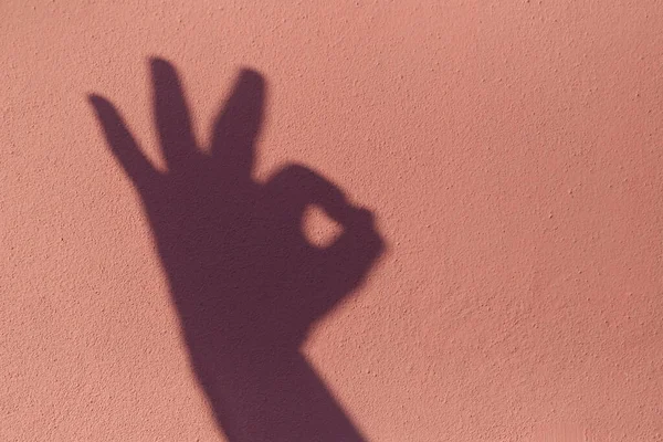 Shadow of the hand that made the ok sign on pink concrete background.