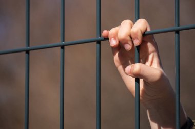 Çocuk mülteci eli metal bir çit tutuyor.