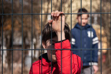 Çocuk mülteci eli metal bir çit tutuyor.