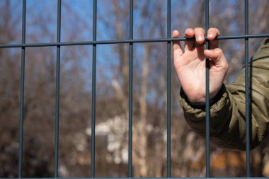 Çocuk mülteci eli metal bir çit tutuyor.