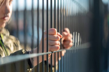 Çocuk mülteci eli metal bir çit tutuyor.