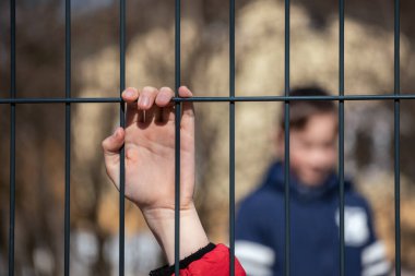 Çocuk mülteci eli metal bir çit tutuyor.