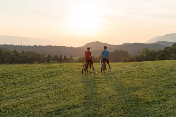Para kolarzy robi sobie przerwę i ogląda zachód słońca w górach, antenę — Zdjęcie stockowe