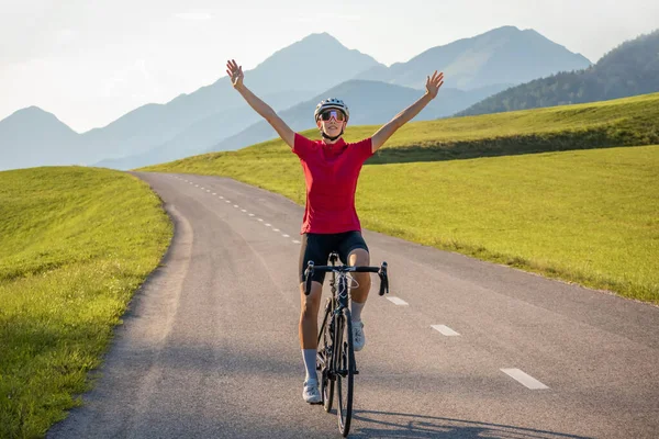 Happy female road racing cyclist in joy, with arms raised