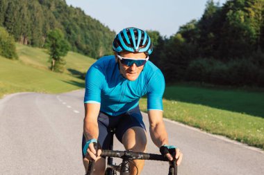 Man in professional cycling clothes riding uphill on an asphalt road