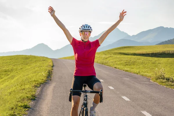 Female cycle race rider raising arms in a victory pose, wide shot