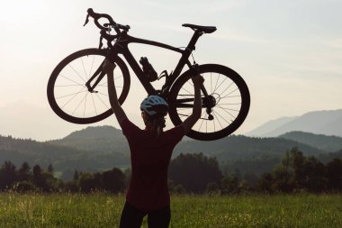 İki kolu başının üstünde bisiklet kaldıran yarışçı bir kadın bisikletçi.